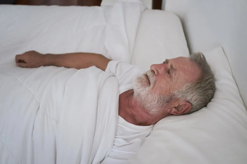 Older man lying awake in bed, staring at the ceiling, a common sign of sleep problems in older adults