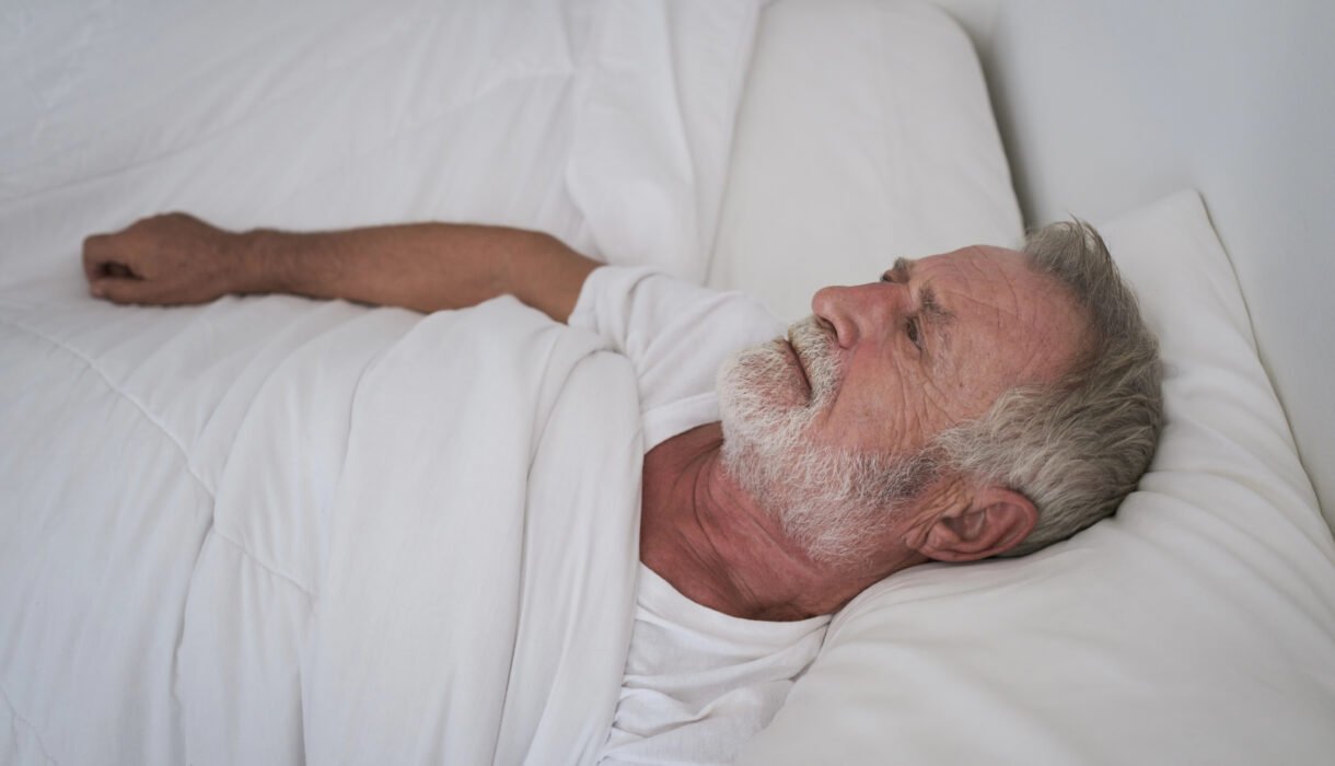 Older man lying awake in bed, staring at the ceiling, a common sign of sleep problems in older adults