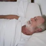 Older man lying awake in bed, staring at the ceiling, a common sign of sleep problems in older adults